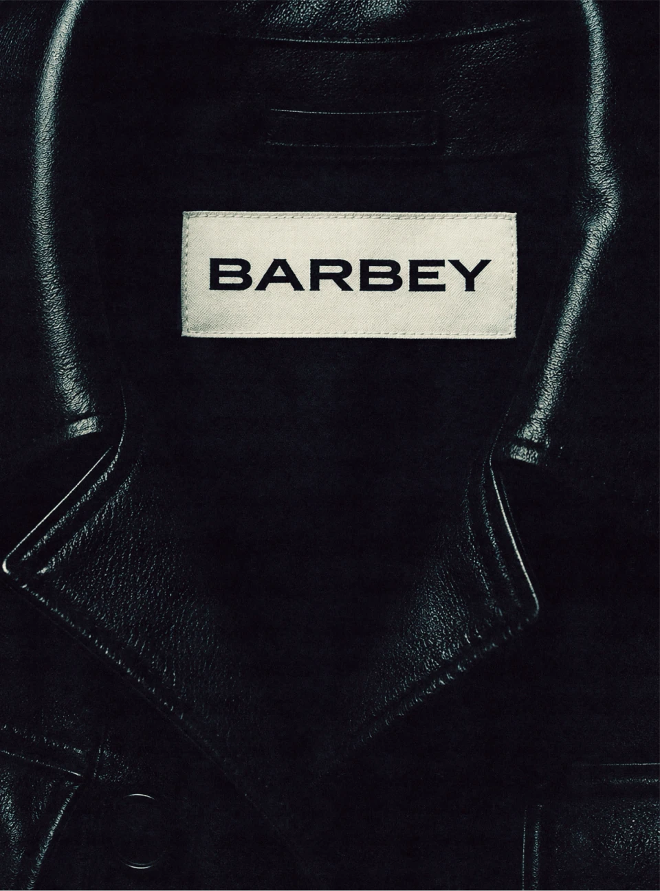 Close-up of a black leather Barbey jacket with a cream woven brand label.
