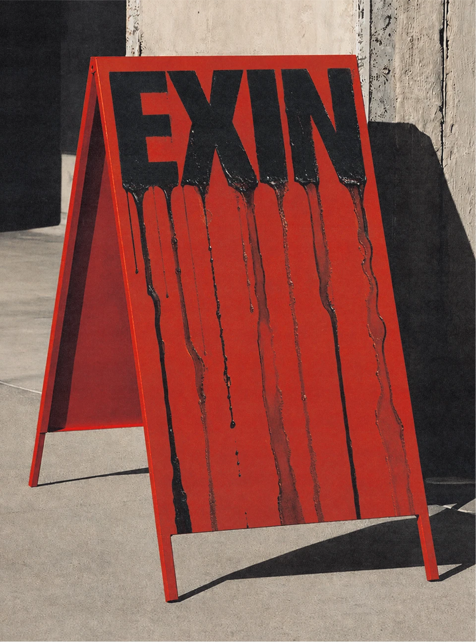 Red freestanding Exin pavement sign photographed on a sidewalk.