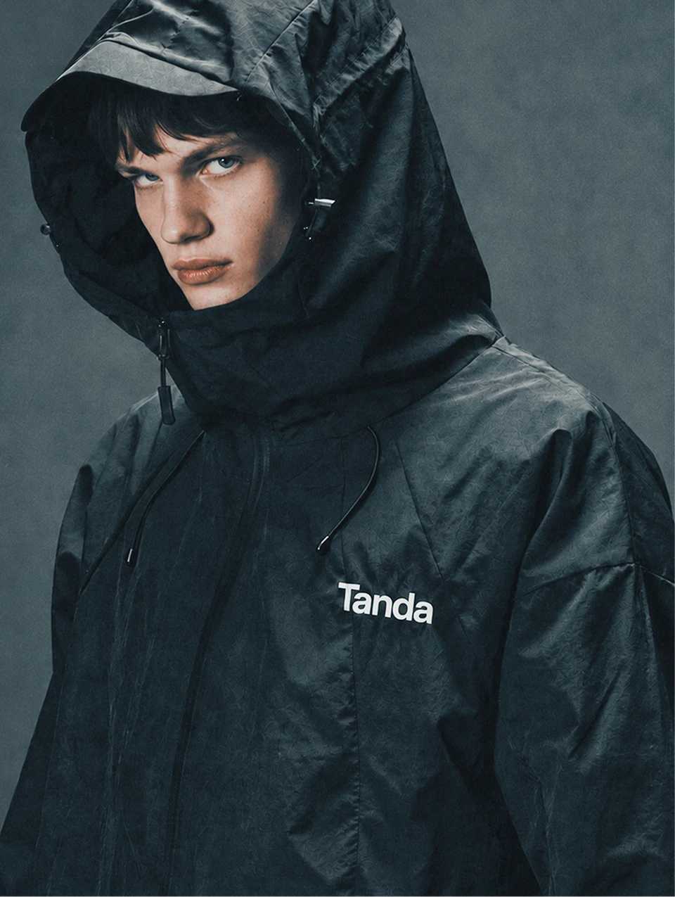 Portrait of a person wearing a black hooded Tanda jacket.