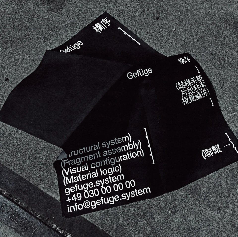 Black Gefüge business cards with white typography and structural-system notation on a textured grey surface.