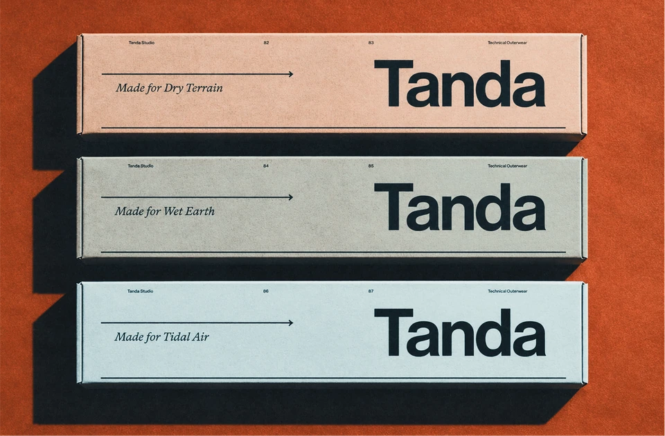 Three slim Tanda packaging boxes in brown, green and blue stacked on orange.